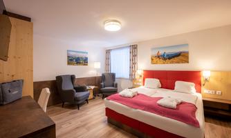 A modern hotel room with a double bed and cozy armchairs. The walls are bright, and there are pictures of landscapes.
