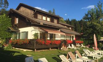 A cozy, two-story wooden house with colorful flower boxes. In the foreground, there are loungers on the lawn.