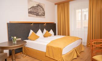 A cozy bedroom with a large bed and yellow accents. The windows let in plenty of daylight and the walls are painted in bright, warm tones.