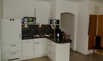A modern kitchen with white furniture and a dark countertop. There is a stove, a sink, and a microwave, as well as a small dining area.