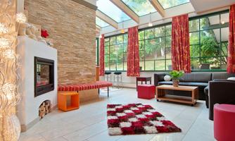 An inviting living room with large windows and plenty of daylight. The modern furnishings include a fireplace, comfortable furniture, and colorful decorative elements.