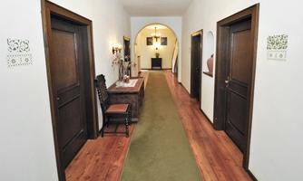A long hallway with wooden doors on both sides and a green carpet in the middle. At the end of the hallway, an arched passage leads into another room.