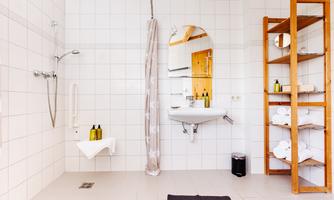 A modern bathroom with white tiles and a shower cubicle. Towels and care products are neatly arranged on a shelf.