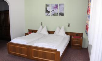 A cozy bedroom with a double bed and two nightstands. Pictures of flowers hang on the wall, and the windows let in plenty of daylight.