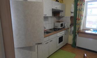 A modern kitchen with bright cabinets and a cooking stove. The windows are decorated with colorful curtains and the floor is covered with a green carpet.