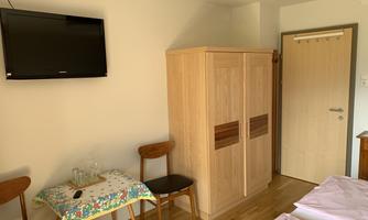 A simple room with two beds, a television, and a wardrobe. There is also a table with two chairs in the corner.