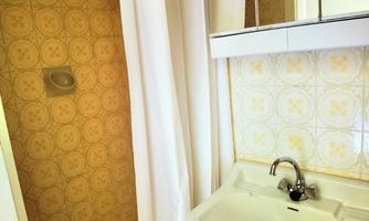 A simple bathroom with a shower and a sink. The walls are decorated with yellow patterned wallpaper.