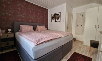A cozy bedroom with a large double bed and pink bedding. The walls are decorated with a decorative pattern, and there is a modern wardrobe.