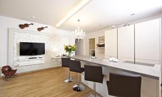A modern kitchen with a long bar counter and elegant bar stools. Decorative violins hang on the wall, and there is a large television as well as a chandelier.