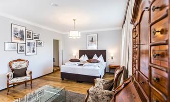 A modern bedroom with a large bed and stylish furniture. The walls are decorated with pictures, and there is a comfortable seating area.