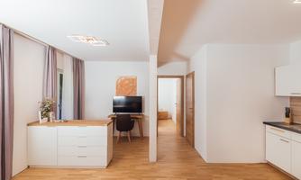 A modern living environment with a bright wooden floor and an open layout. In the background, there is a desk with a computer.