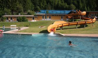 A fun pool with a water slide and a clear swimming pool. In the background, there are loungers and a building visible.