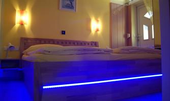 A modern bedroom with a large bed and a yellow color scheme. Soft lighting and blue LED lights create a cozy atmosphere.