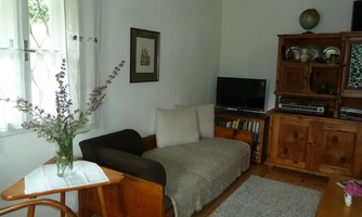 A cozy living room with a sofa and a small table. On the table sits a vase with fresh flowers, and in the background, a bookshelf can be seen.
