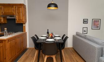 A modern dining room with a wooden kitchen area and an elegant table. The room is bright and inviting, with stylish chairs and a comfortable couch.