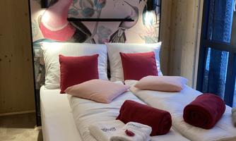 A cozy bedroom with a modern bed and colorful pillows. The walls are decorated with intricate, floral-inspired motifs.