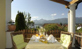 A cozy balcony with a table set for breakfast. In the background, mountains and a clear sky can be seen.