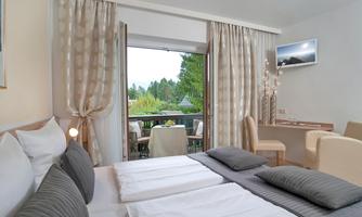A modern bedroom with two beds and cozy furnishings. The view overlooks a balcony with a beautiful view of the greenery.