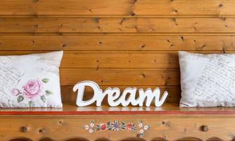 A wooden wall background with a lovingly decorated table. On it are cushions and the word "Dream" in white lettering.