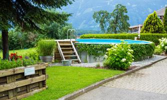 A beautiful garden with a swimming pool and well-maintained lawn. In the background, mountains and trees can be seen.