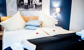 A cozy bedroom with a large bed and decorative pillows. Two small red hearts are placed on the bedspread.