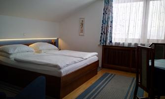 A cozy bedroom with a double bed and bright windows. The room is simply and modernly furnished.
