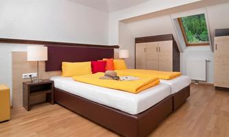 A cozy bedroom with a large double bed and colorful cushions. There is wooden flooring and plenty of daylight through the window.