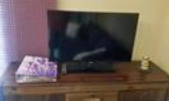 A television is standing on a wooden table. Next to the television lies a gift box and a small decoration.