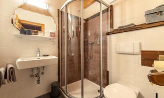 A modern bathroom with a shower cubicle and a sink. The walls are brightly tiled and there is a wooden shelf for additional storage.