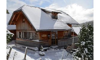 A cozy wooden house in the snowy winter forest. The surroundings are filled with fresh snow and green fir trees.