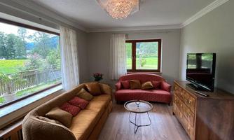 A cozy living room with a brown sofa and a red sofa. Large windows offer a view of the garden outside.