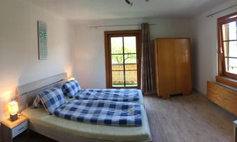 A bright bedroom with two single beds and checkered bedcovers. Large windows provide plenty of daylight and a view of the outdoors.