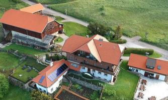 A rural scene with several buildings and rooftop gardens. Surrounded by green fields and trees.