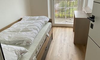 A cozy bedroom with a bed and wooden floor. There is a beautiful view of the surroundings through the window.