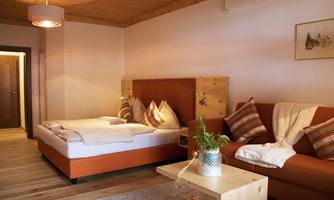 A cozy room with a double bed and an orange couch. The room has wooden details and an inviting atmosphere.