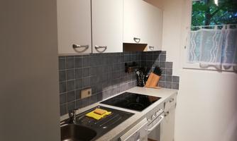 A modern kitchen with white cabinets and a gray tile wall. On the countertop, cooking utensils and a dish towel can be seen.