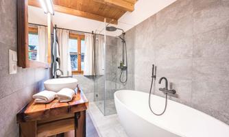 A modern bathroom with a freestanding bathtub and a separate shower. The wood paneling and large windows create a bright, inviting atmosphere.