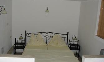 A simple bedroom with a double bed and two nightstands. The walls are white and the lighting is soft.