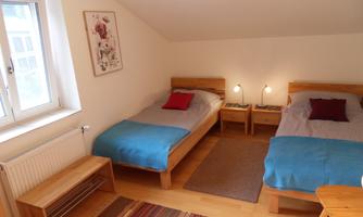 A cozy bedroom with two single beds and warm colors. Natural light streams through the window, creating an inviting atmosphere.