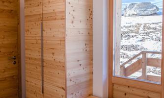 A modern entrance area with a wooden wardrobe and a bench. Through the window, you can see a mountain landscape.