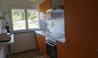 A modern kitchen with orange cabinets and a view of nature. The window lets in plenty of light and creates an inviting atmosphere.