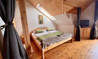 A cozy bedroom with a double bed and wooden ceiling. The furnishings are simple and rustic, with a wardrobe and a television.