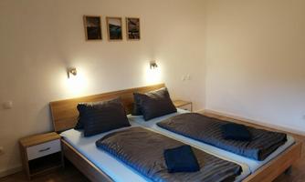 A modern bedroom with a large bed and two pillows. Three pictures hang on the wall, and there are nightstands with lamps.