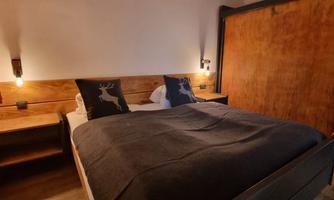 A modern bedroom with a large bed and wooden details. The soft lighting creates a cozy atmosphere.