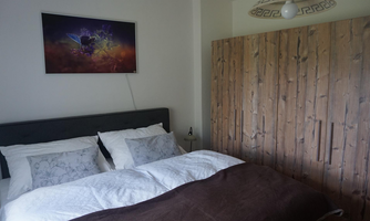 A cozy bedroom with a large bed and modern pillows. A colorful picture hangs on the wall, and a wooden wardrobe stands next to the bed.