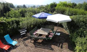 A cozy garden with a large table and colorful chairs. Two sun umbrellas provide shade in a green setting.