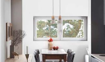 A modern dining area with a wooden table and black chairs. Bright walls and large windows create a friendly atmosphere.