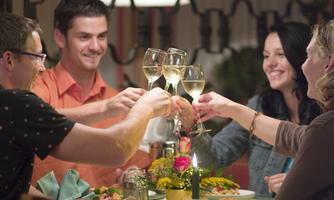 A group of four friends is celebrating at dinner. They are toasting with glasses and enjoying delicious dishes.