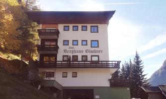 A multi-story building named "Berghaus Glockner" can be seen. It is located in a picturesque mountain landscape with trees in autumn.