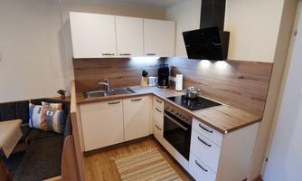A modern kitchen with wooden shelves and silver fixtures. It is well-lit and features a dining area.
